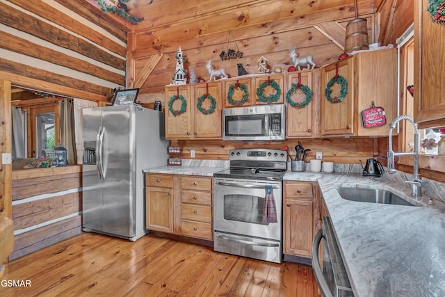 kitchen with light wood-type flooring, stainless steel appliances, wood walls, and sink