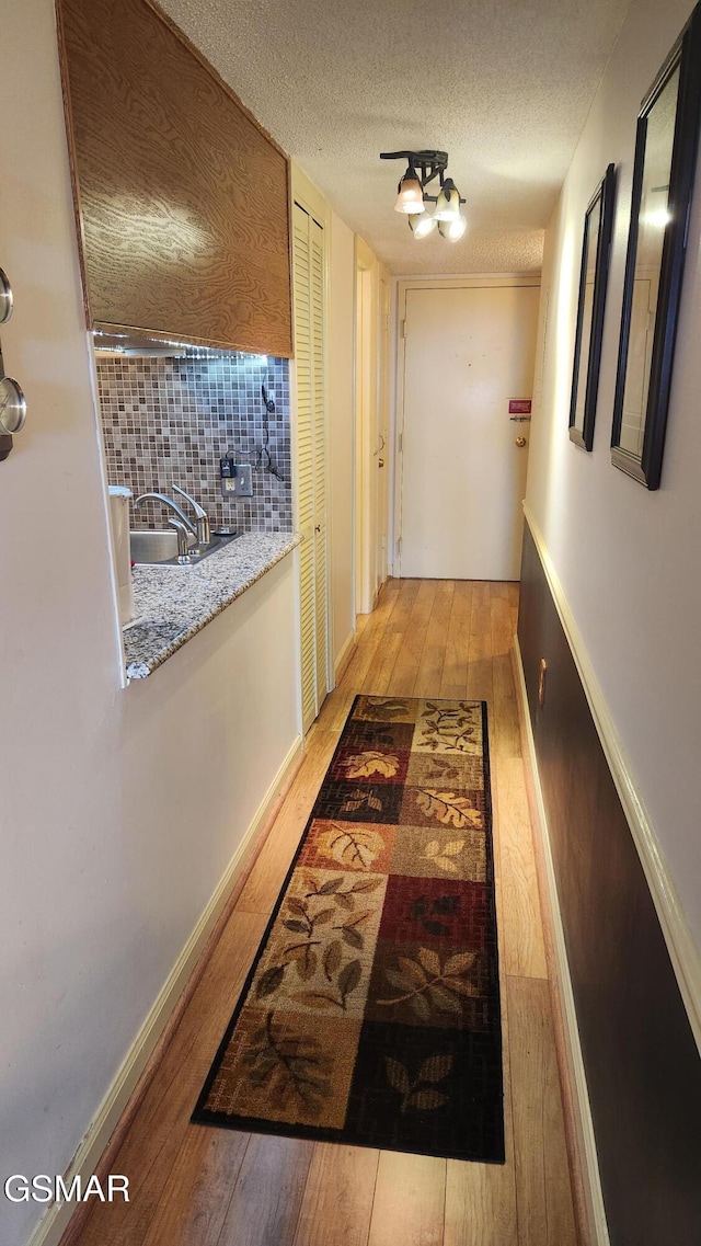 corridor with light wood-type flooring, a textured ceiling, and sink