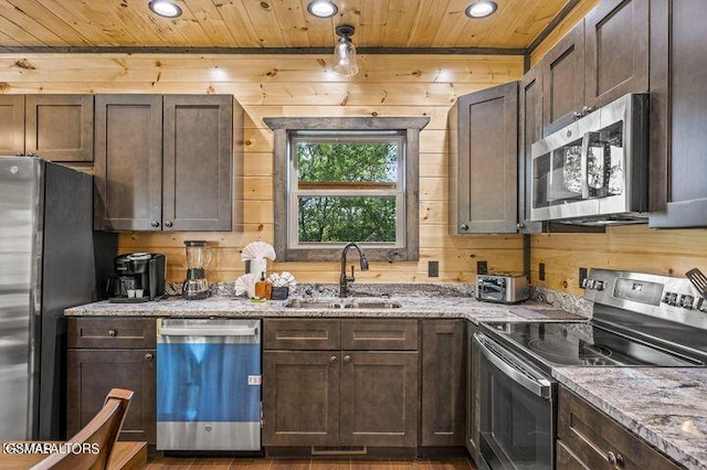 kitchen featuring wooden ceiling, wooden walls, a sink, appliances with stainless steel finishes, and light stone countertops