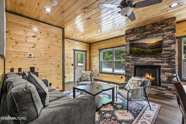 living area featuring wooden walls, wooden ceiling, a stone fireplace, and wood finished floors