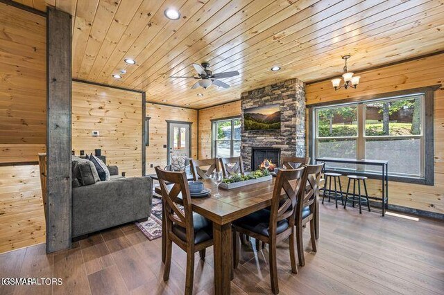 dining room with wooden ceiling, a stone fireplace, wood finished floors, and wood walls