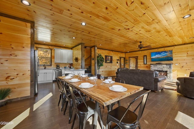 dining space with wood walls, dark wood-style flooring, a fireplace, wood ceiling, and a ceiling fan