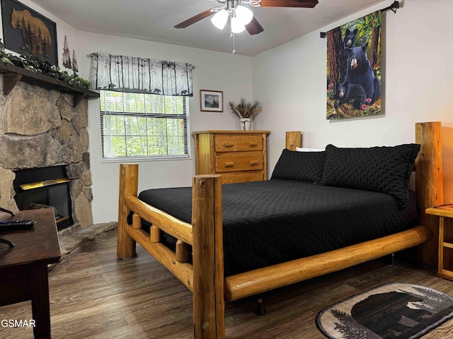 bedroom featuring ceiling fan, a stone fireplace, and wood finished floors