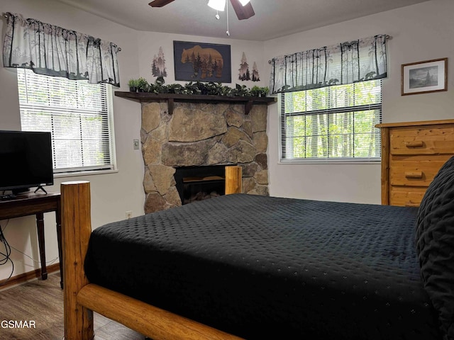 bedroom with ceiling fan, wood finished floors, and a fireplace