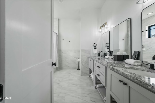 bathroom with marble finish floor, a sink, tile walls, and double vanity