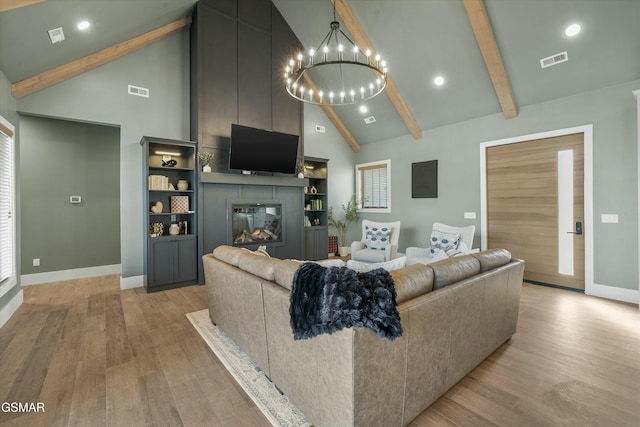 living area featuring a large fireplace, light wood finished floors, visible vents, an inviting chandelier, and beam ceiling