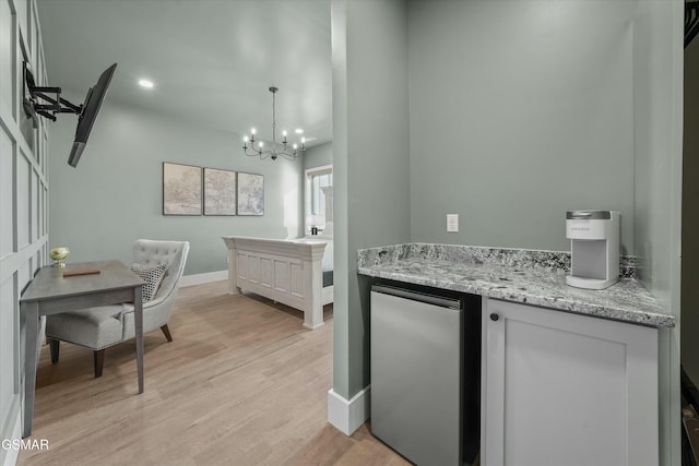 kitchen featuring light stone counters, light wood finished floors, an inviting chandelier, baseboards, and fridge