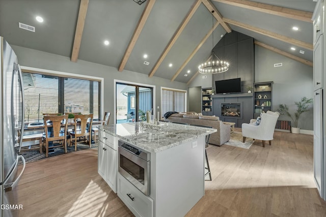 kitchen featuring a center island with sink, visible vents, white cabinets, stainless steel appliances, and a fireplace