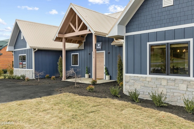 view of front of property featuring stone siding, metal roof, board and batten siding, and a front yard