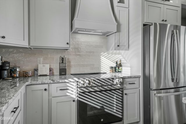 kitchen with custom exhaust hood, stainless steel appliances, backsplash, glass insert cabinets, and light stone countertops