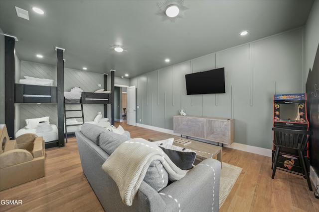 living area featuring recessed lighting, visible vents, a decorative wall, and wood finished floors