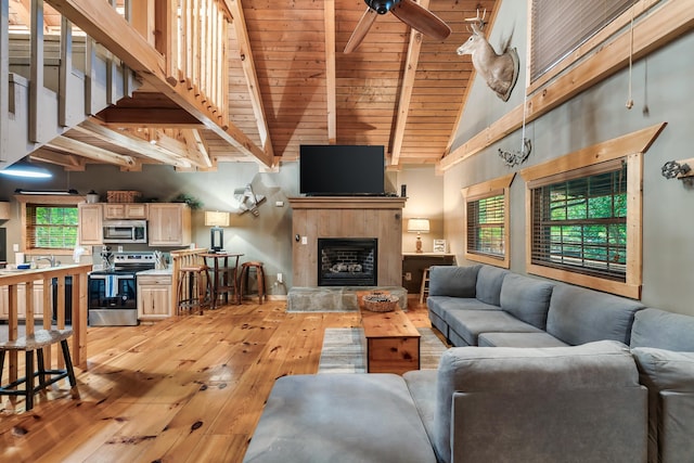 living area featuring a fireplace, light wood finished floors, ceiling fan, high vaulted ceiling, and beamed ceiling