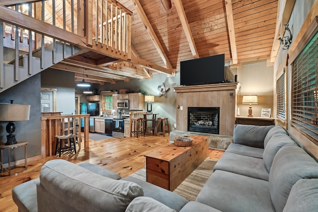 living area featuring light wood-style floors, a fireplace with raised hearth, and beamed ceiling