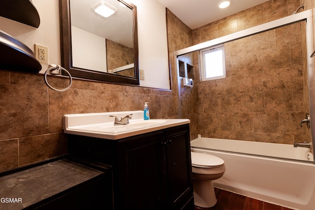 bathroom with tile walls, wood finished floors, vanity, toilet, and shower / bathtub combination