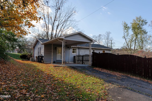 bungalow-style house with aphalt driveway, fence, cooling unit, an attached carport, and a gate