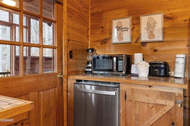 kitchen featuring wooden walls, stainless steel microwave, tile counters, and refrigerator