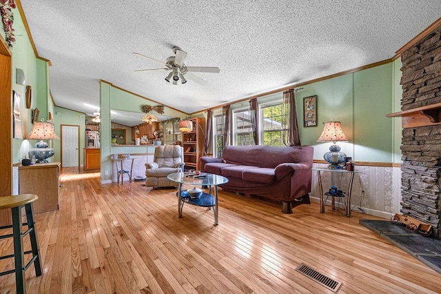 living room featuring light wood-type flooring, vaulted ceiling, ceiling fan, a stone fireplace, and wood walls