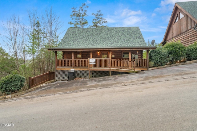 log home featuring covered porch, log exterior, a shingled roof, and concrete driveway