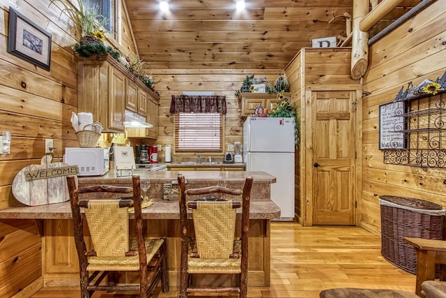 kitchen featuring kitchen peninsula, white fridge, and wood walls