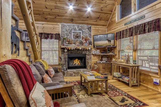 living area featuring wooden walls, wood-type flooring, high vaulted ceiling, wooden ceiling, and a stone fireplace