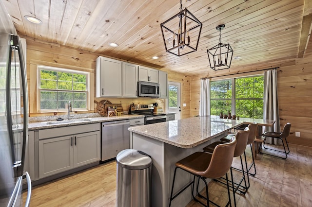 kitchen featuring pendant lighting, sink, wooden walls, appliances with stainless steel finishes, and a kitchen island