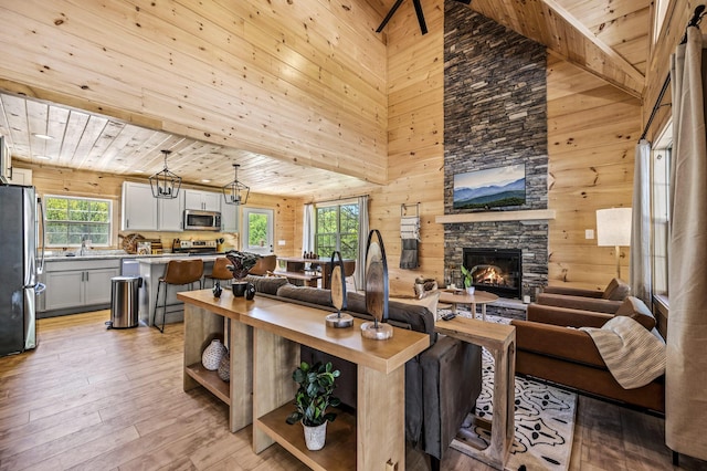 living room featuring plenty of natural light, a stone fireplace, wooden ceiling, and light hardwood / wood-style flooring