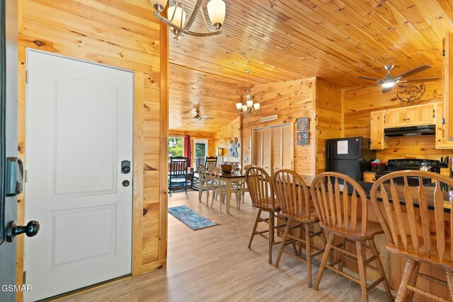 dining space featuring wood ceiling, ceiling fan with notable chandelier, vaulted ceiling, wooden walls, and light hardwood / wood-style flooring