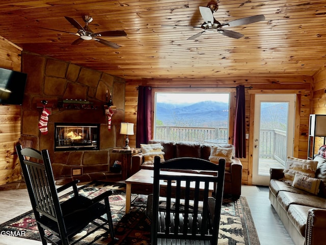 living room featuring hardwood / wood-style floors, wooden ceiling, a stone fireplace, vaulted ceiling, and ceiling fan