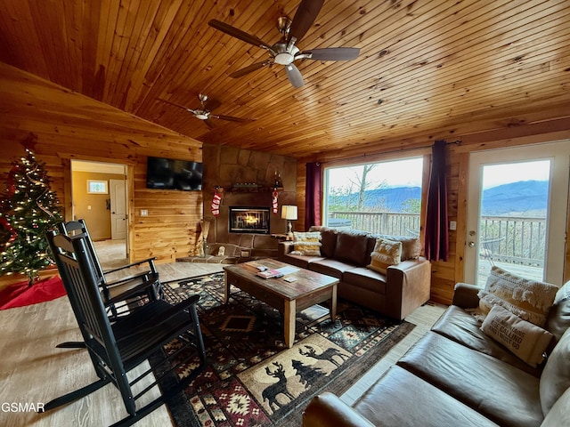 living room with ceiling fan, wooden ceiling, a stone fireplace, lofted ceiling, and wooden walls