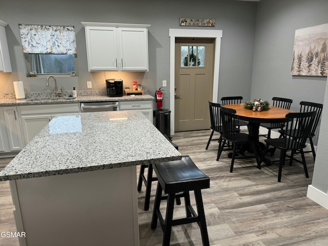 kitchen with light wood-style floors, white cabinetry, a center island, dishwasher, and a sink