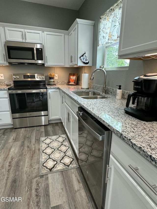 kitchen with white cabinets, wood finished floors, light stone counters, a sink, and stainless steel appliances