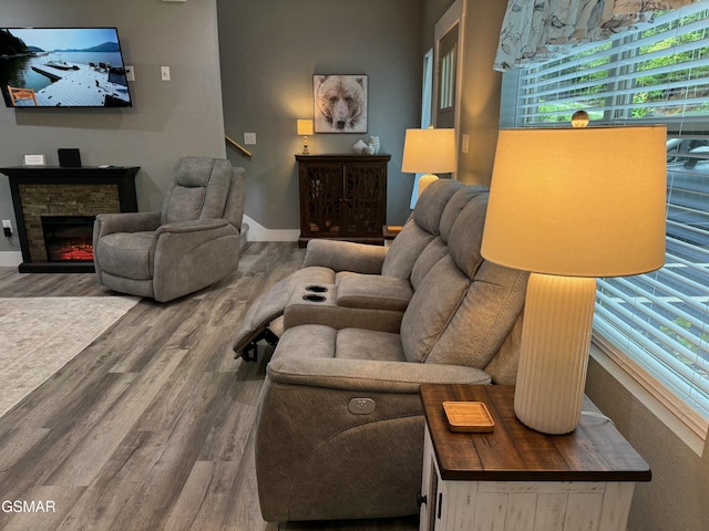 living area with a stone fireplace, baseboards, and wood finished floors