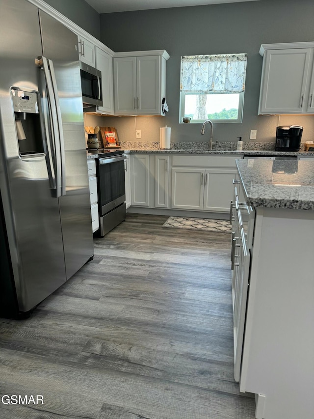 kitchen featuring light stone countertops, white cabinets, appliances with stainless steel finishes, wood finished floors, and a sink
