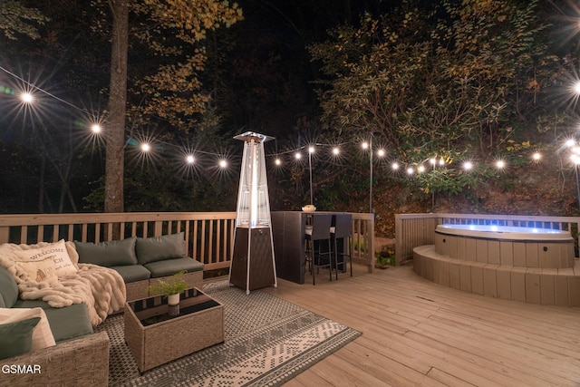 deck at night with a hot tub and an outdoor living space