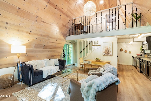 living area with high vaulted ceiling, wood walls, wood ceiling, stairs, and light wood finished floors