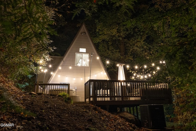 back of house at night with a deck and cooling unit