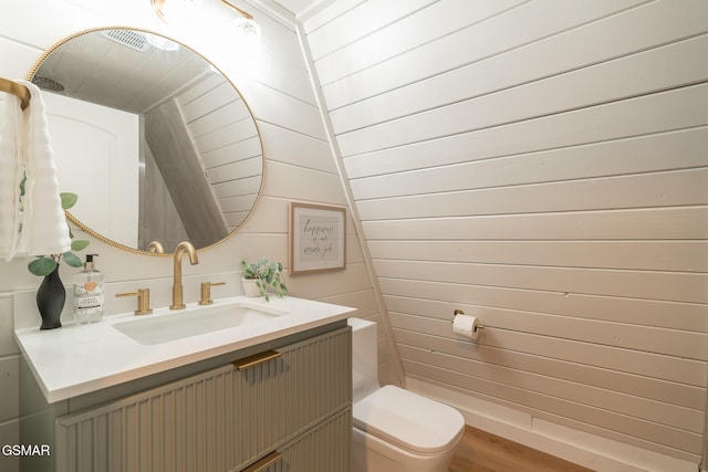 bathroom with toilet, wood finished floors, vanity, and wooden walls