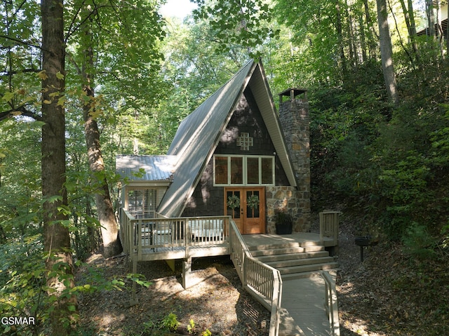 rear view of house featuring a deck, a chimney, metal roof, and french doors