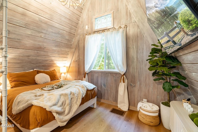 bedroom featuring visible vents, vaulted ceiling, wooden walls, and wood finished floors