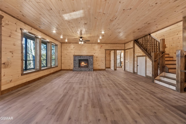 unfurnished living room featuring ceiling fan, wooden ceiling, hardwood / wood-style floors, a stone fireplace, and wood walls