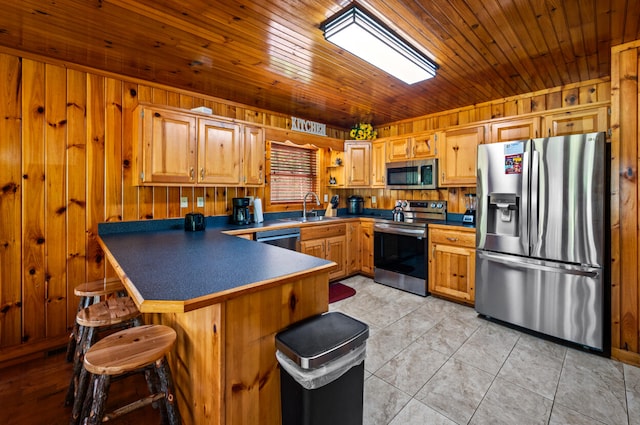 kitchen featuring a breakfast bar, stainless steel appliances, sink, wood walls, and light tile patterned flooring