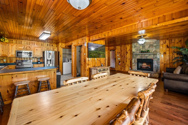 dining area featuring a stone fireplace, wooden walls, dark hardwood / wood-style floors, and washer / dryer