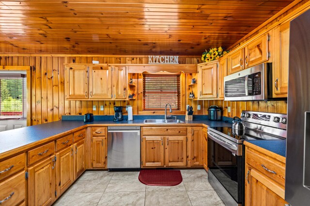 kitchen with light tile patterned floors, stainless steel appliances, wood walls, and sink