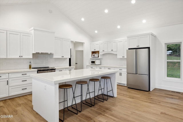 kitchen with appliances with stainless steel finishes, light hardwood / wood-style flooring, high vaulted ceiling, a center island, and white cabinetry