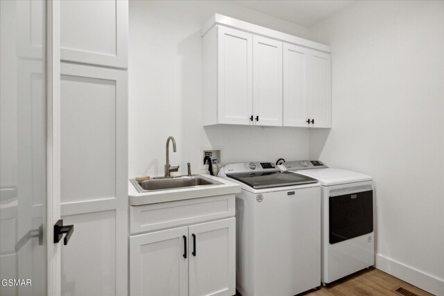 clothes washing area with washer and dryer, sink, cabinets, and light hardwood / wood-style flooring