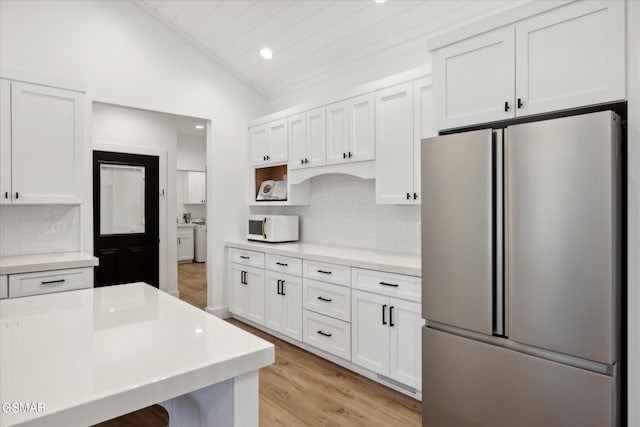 kitchen featuring white cabinets, vaulted ceiling, separate washer and dryer, tasteful backsplash, and stainless steel refrigerator