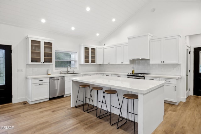 kitchen featuring appliances with stainless steel finishes, a kitchen island, wall chimney range hood, sink, and white cabinetry