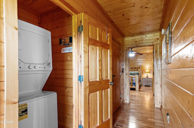 clothes washing area with stacked washer and dryer, laundry area, wooden ceiling, light wood-style flooring, and wood walls