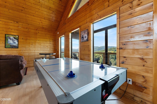 recreation room featuring light wood-type flooring, high vaulted ceiling, wooden walls, and a mountain view