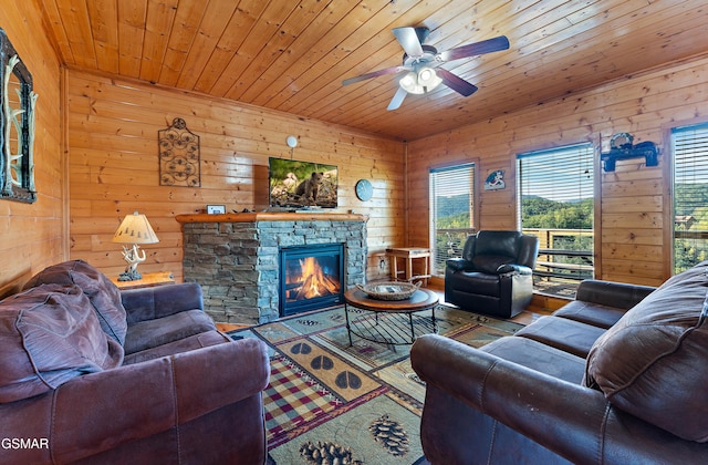 living area with wood ceiling, ceiling fan, a stone fireplace, and wood finished floors